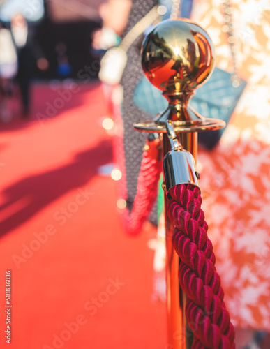 Red carpet with ropes and golden barriers on a luxury party entrance, cinema premiere film festival event gala ceremony, wealthy rich guests ariving, outdoor decoration elements, summer sunny day photo