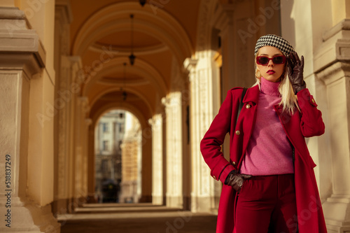Fashionable confident blonde woman wearing trendy sunglasses, beret, pink turtleneck cashmere sweater, dark red color autumn coat, gloves, posing in street of European city. Copy, empty space for text