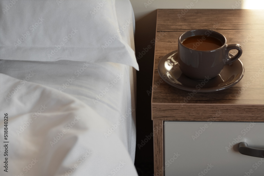 Cup of morning coffee on wooden night stand near bed indoors