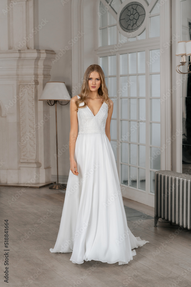The beautiful woman posing in a wedding dress. Young beautiful happy bride wearing white wedding dress and posing in bright empty interior. Wedding fashion. Expensive Lace bust. The beautiful woman posing in a wedding dress. Young beautiful happy bride wearing white wedding dress and posing in bright empty interior. Wedding fashion. Expensive Lace bust.
