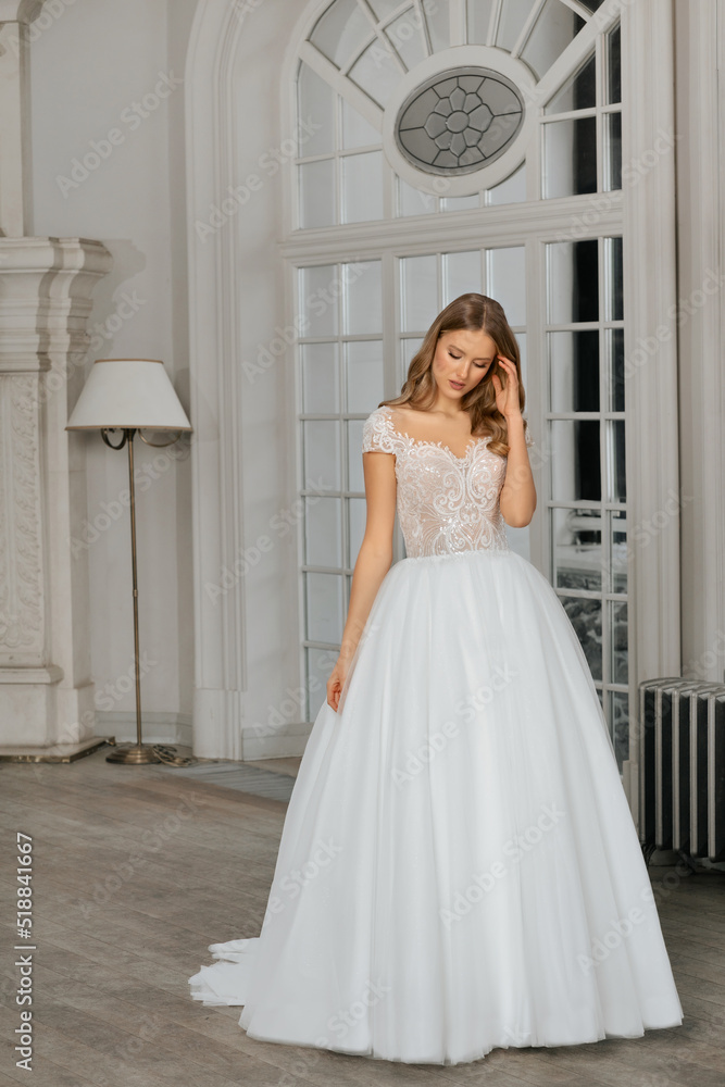 The beautiful woman posing in a wedding dress. Young beautiful happy bride wearing white wedding dress and posing in bright empty interior. Wedding fashion. Expensive Lace bust. The beautiful woman posing in a wedding dress. Young beautiful happy bride wearing white wedding dress and posing in bright empty interior. Wedding fashion. Expensive Lace bust.