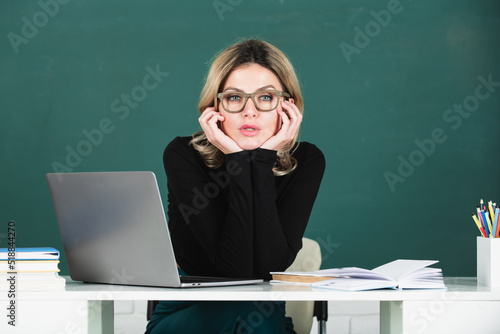 Portrait of teacher at school with computer laptop in classroom on blackboard.
