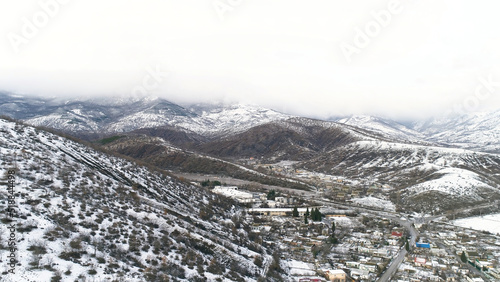 Winter landscape with snowy fields, trees, and village on cloudy sky background. Shot. Aerial for snowy mountain slopes, forest, and rare houses.