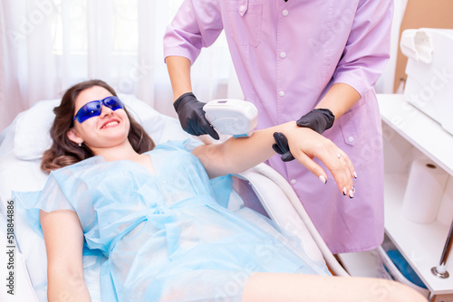 Laser hair removal procedure in a beauty salon. The master cosmetologist removes hair on the patient s face and body using a laser device. Depilation of legs  arms  armpits and bikini area.