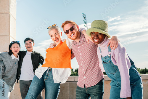 Portrait of multiracial friends hugging and smiling in front of the camera in a sunny day.