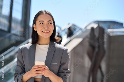 Obraz na plátně Happy young Asian business woman standing on urban street using cell phone