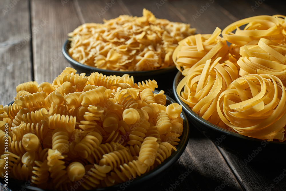 Three deep bowls with uncooked pasta on a wooden table. Assortment of raw macaroni Three deep bowls with uncooked pasta on a wooden table. Assortment of raw macaroni