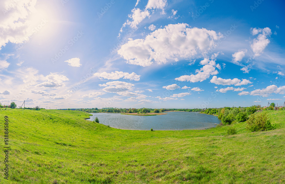 Obraz premium Green field and blue pond in the village Vchorayshe, Zhytomyr Region, Ukraine