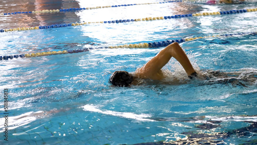 Man Swimming in Pool. Fit young male swimmer training in the pool. Young man swimming the front crawl in a pool. Young male athlete swimming freestyle in pool during competition © Media Whale Stock