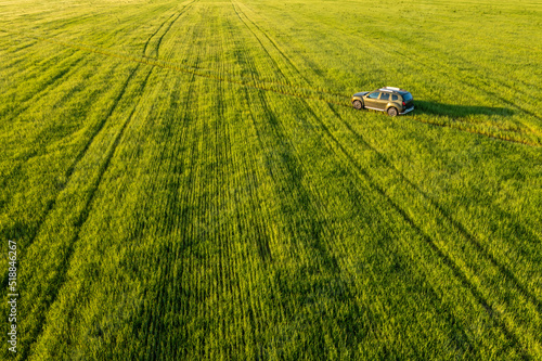 Aerial view of car SUV parked near countryside road in field rural landscape. Bird's-eye drone view of car SUV parked near countryside road in summer field rural landscape. 