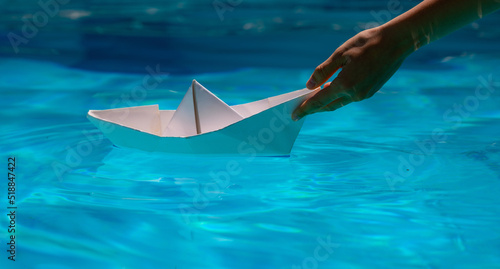 Paper boat with hand. Paper boat sailing on blue water surface. Origami paper boat.