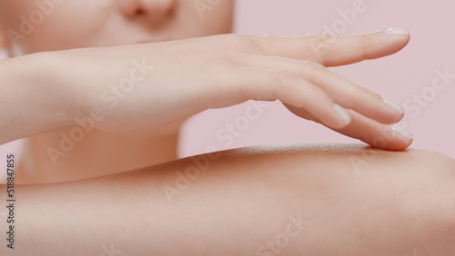 Good-looking young slim Caucasian woman strokes her forearm on pale pink background | Unwanted arm hair removal concept