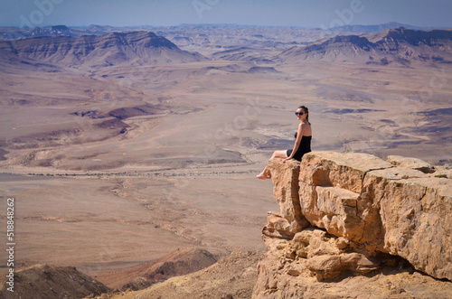 Girl siting on a cliff looking at desert Negev landscape. Summer vacation in Israel