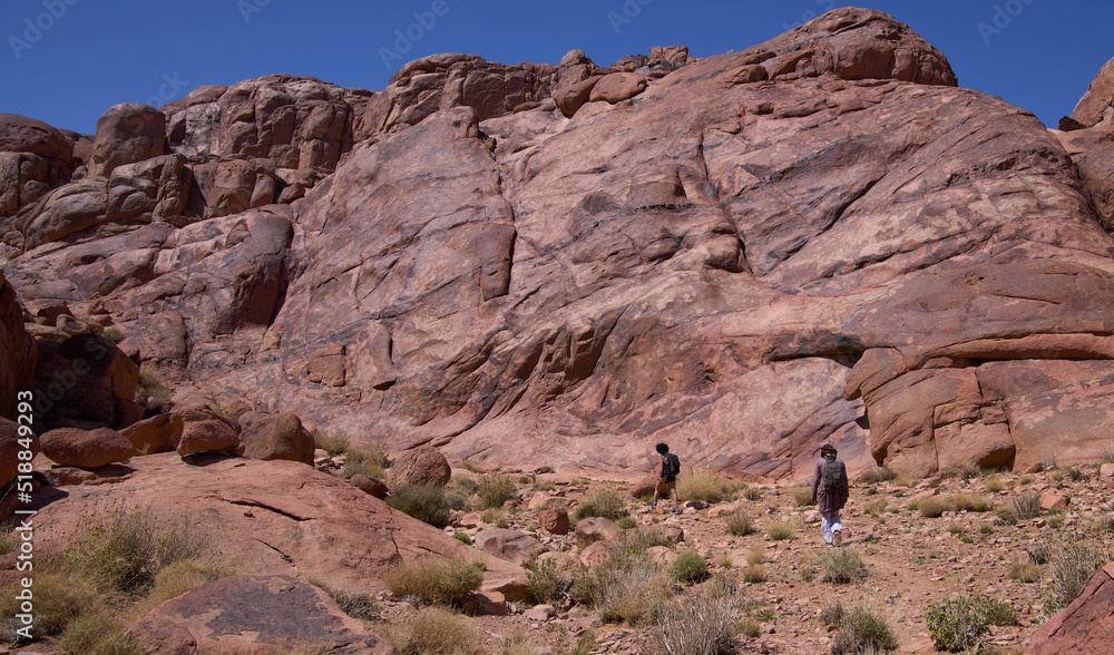 Local bedouin and female hiker on the hiking trail  in the Southern Sinai, Egypt. Panoramic view over the trail on surrounding red mountains.