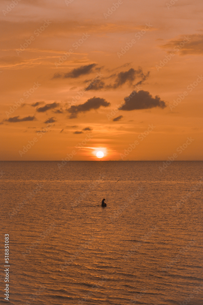 Persona pescando en el mar durante una puesta de sol