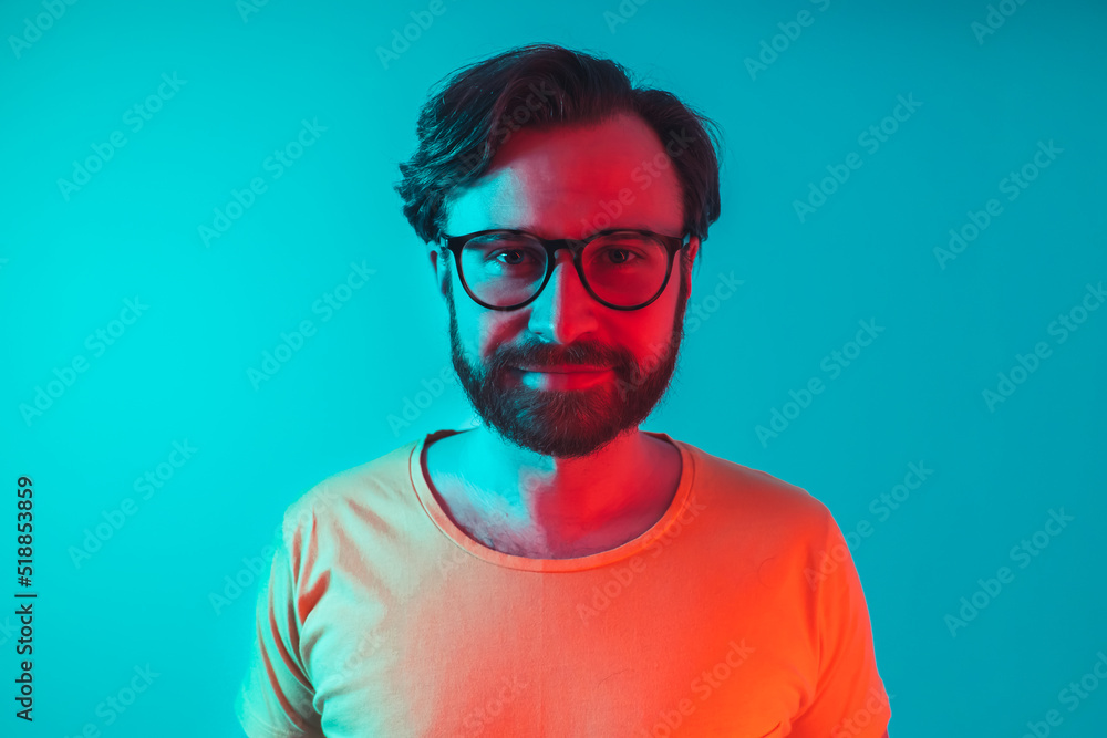 Medium shot of young Millenial looking into the camera in studio environment - red and turquoise neon lights. High quality photo