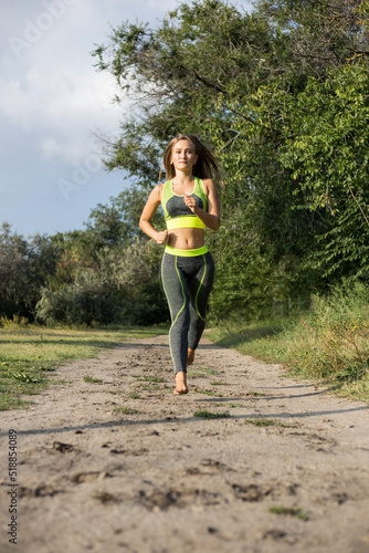 Young blonde girl runs barefoot in the forest. Running woman, side view. Jogging in the park