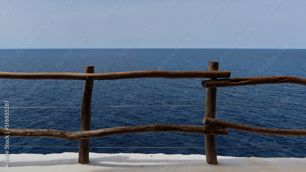 Wooden railings over the precipice. Safety railing on the cliff. Panoramic sea view. Menorca, Spain. Selective focus Wooden railings over the precipice. Safety railing on the cliff. Panoramic sea view. Menorca, Spain. Selective focus
