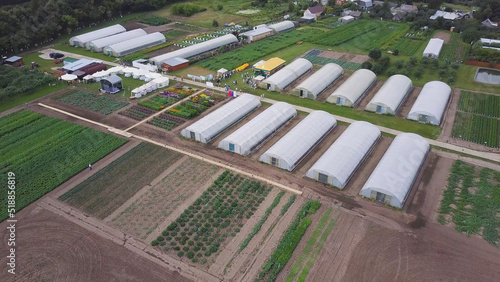 Aerial drone shot of a green house surrounded by agricultural land. Clip. Aerial view on countryside. Farm workers getting ready for growing vegetables, fruits and herbs. Vegetable Fields and