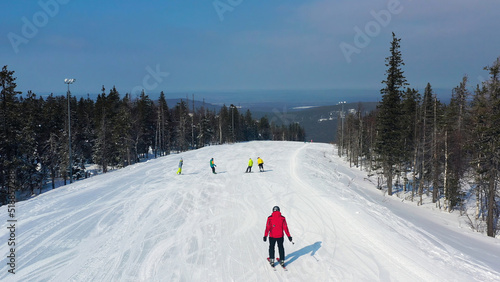 Modern ski resort in pine forest aeria, view from above. Footage. Young group of people snowboarding and skiing down the snowy slope. photo