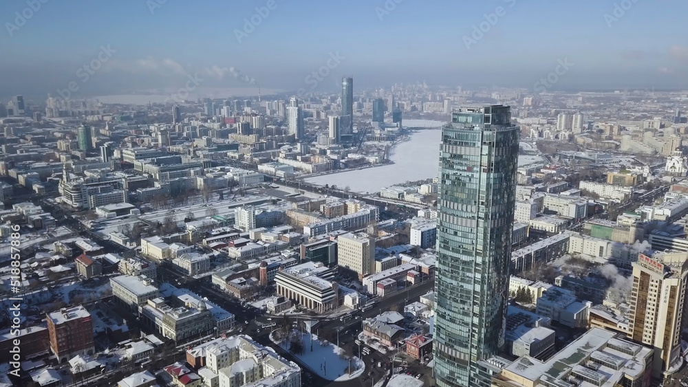 Top view of the amazing glass tower or the business center in the background of a winter city. Aerial view of skyscraper is in the middle of the city in winter, blue sky sky and snowy roofs of