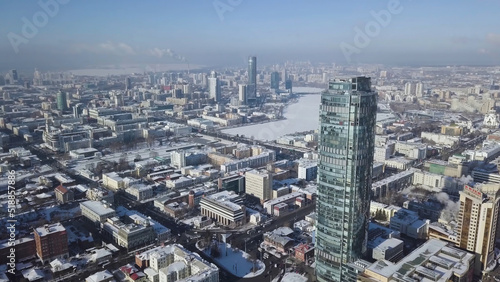 Top view of the amazing glass tower or the business center in the background of a winter city. Aerial view of skyscraper is in the middle of the city in winter  blue sky sky and snowy roofs of