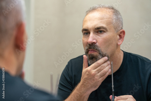 Middle-aged handsome man using scissors to cut his beard a litlie and fix the shape photo