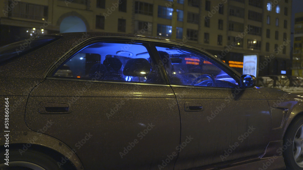 Side view of a modern vehicle with beautiful purple shining car body covering moving fast in the city at night. Action. Tuned passenger car with neon blue light driving along the streets.