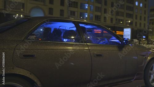 Side view of a modern vehicle with beautiful purple shining car body covering moving fast in the city at night. Action. Tuned passenger car with neon blue light driving along the streets. © Media Whale Stock