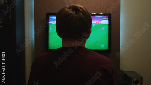 Young man watching football game via tv at home. Concept. Rear view of a man sitting on a couch at home and watching football late in the evening.