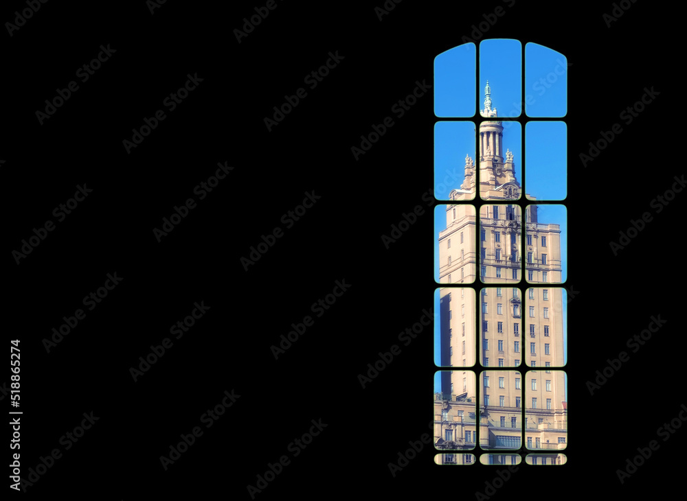 View from inside big window grid looking out at a traditional skyscraper building on blue sky copy space. Dark room with light part of a gothic vintage tower. Architecture of a tall built structure