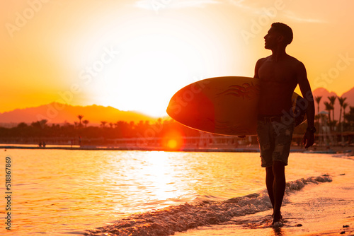Silhouette man surfer in sunset light walking down beach with surfboard near waters edge enjoying summer time practice hobby during getaway vacations, guy recreating at tropical island with waves