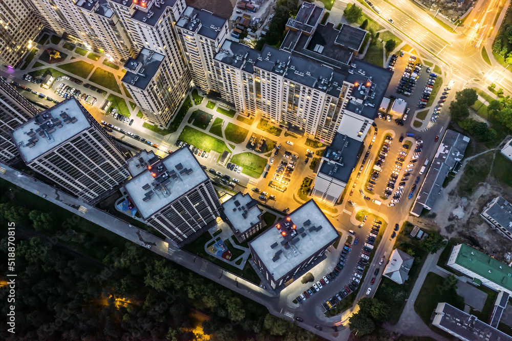 illuminated apartment buildings complex near city park at night. courtyard with parked cars. aerial drone photo looking down.