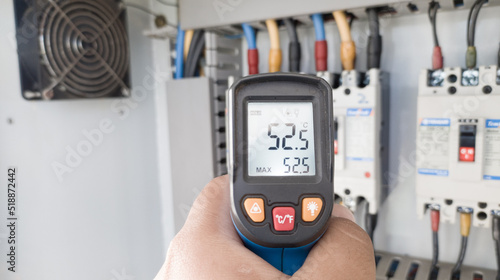 an electrician is using a thermogun to analyze sub-wires and components, use digital infrared thermometer to find out overcurrent loads, and abnormalities in the panel's electrical system.