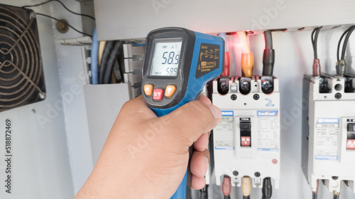 an electrician is using a thermogun to analyze sub-wires and components, use digital infrared thermometer to find out overcurrent loads, and abnormalities in the panel's electrical system. photo