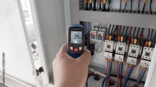 an electrician is using a thermogun to analyze sub-wires and components, use digital infrared thermometer to find out overcurrent loads, and abnormalities in the panel's electrical system. photo