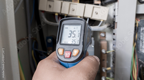 an electrician is using a thermogun to analyze sub-wires and components, use digital infrared thermometer to find out overcurrent loads, and abnormalities in the panel's electrical system. photo