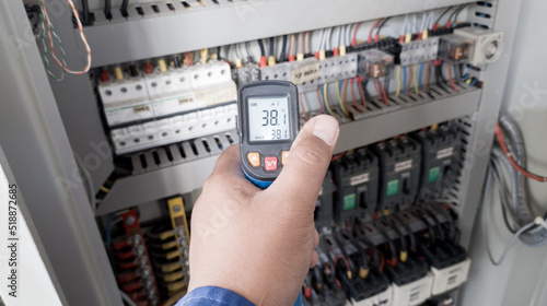 an electrician is using a thermogun to analyze sub-wires and components, use digital infrared thermometer to find out overcurrent loads, and abnormalities in the panel's electrical system.