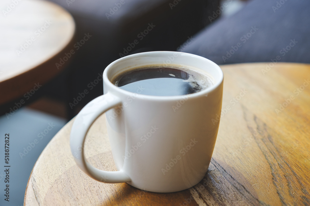 Closeup image of a white cup of hot coffee on wooden table in cafe Closeup image of a white cup of hot coffee on wooden table in cafe