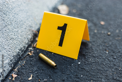 One yellow crime scene evidence marker on the street after a gun shooting brass bullet shell casing rifle