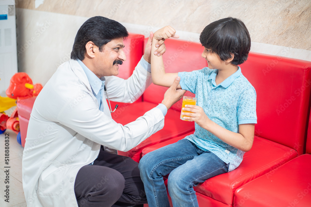 Happy male indian doctor cheer support boy patient at visit to clinic, kid hold glass of juice, Caring pediatrician have fun with little child in hospital. Children healthcare concept. Happy male indian doctor cheer support boy patient at visit to clinic, kid hold glass of juice, Caring pediatrician have fun with little child in hospital. Children healthcare concept.