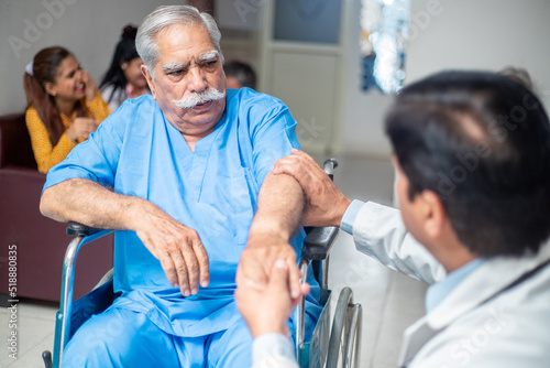 Indian male doctor check disabled elder patient sit on wheelchair at home hospital, paralyzed old people treatment and therapy, healthcare. photo