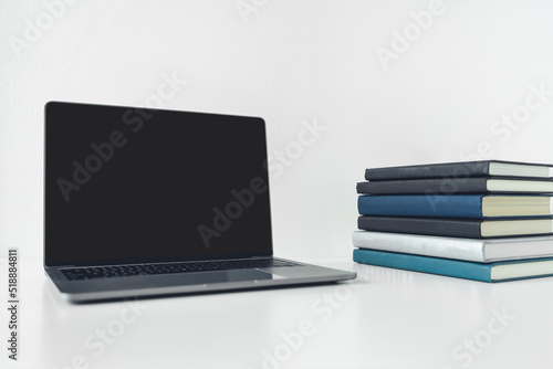 Laptop mock up with blank or empty screen with book or textbook stack with copy space. Using computer notebook for business working or education learning online via internet or cyberspace