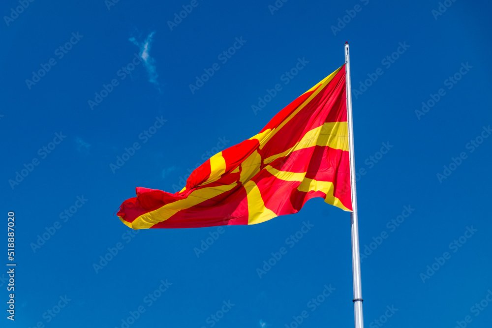 Flag of North Macedonia on blue sky. Stylised yellow sun on a red field on flag.