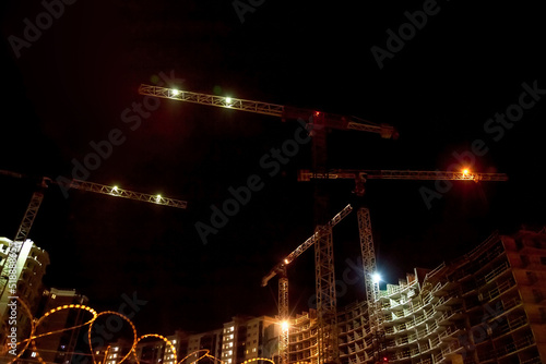 Building construction site with cranes and light flare at  night time background