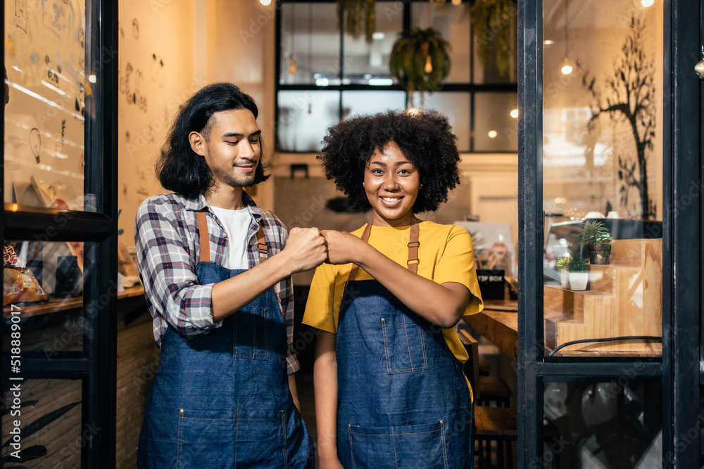 Obraz premium Young couple asian man and african woman manager in restaurant with digital tablet or notebookWoman coffee shop owner with face mask hold open sign .Small business concept.