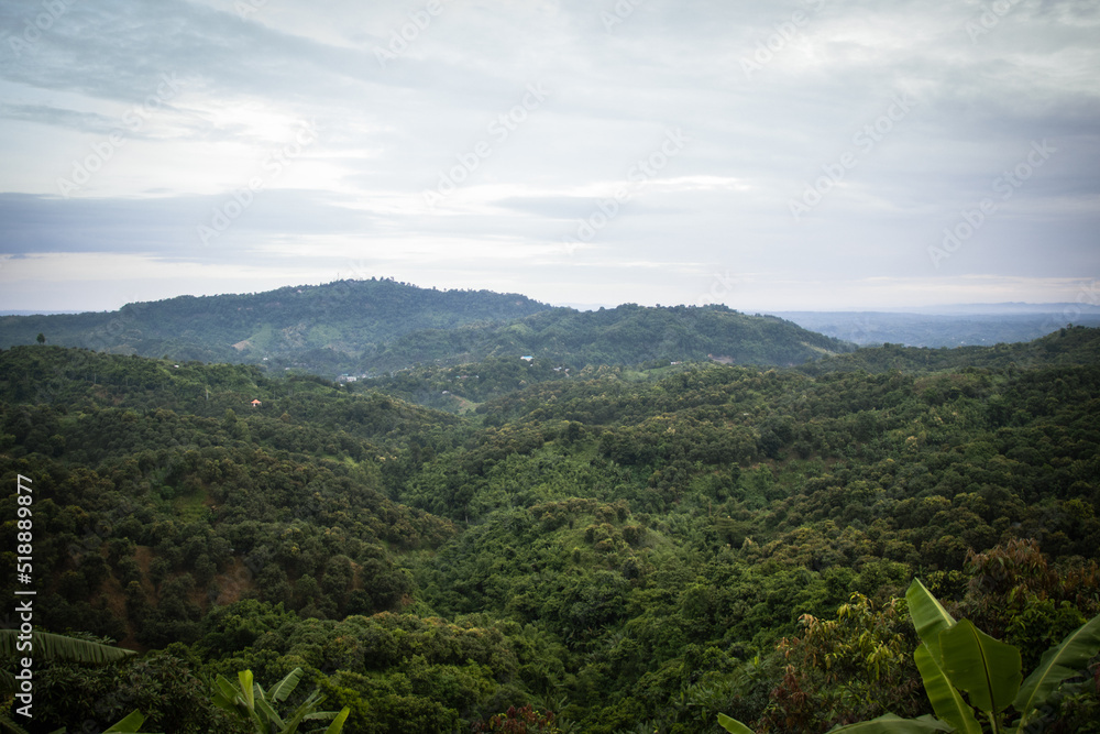 Obraz premium Country landscape with rural forest and cloud. Green hill area with the horizon view. Hilly jungle area with small buildings at Bandarban, Bangladesh. Village area with a beautiful sky for tourists.