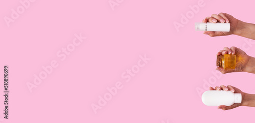 Female hands with different cosmetic products in container and bottle on pink color background with copy space