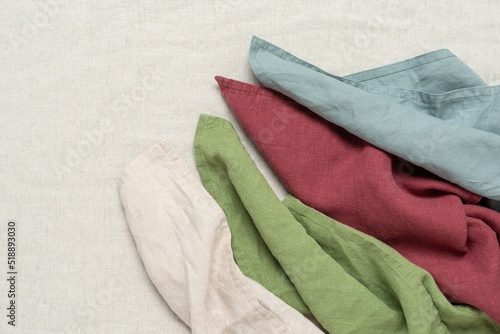 Colorful linen napkins flat lay on a beige linen background. View from above. Concept of eco-friendly fabrics.