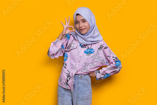 young asian beautiful muslim woman with ok sign gesture tumb up isolated on yellow background  © dwi